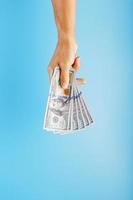 A hand with one hundred-dollar bills on a blue background. photo