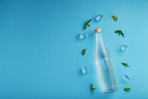 Bottle with an ice cold beverage, ice cubes, drops and mint leaves on a blue background. photo