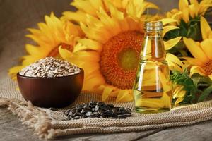 Sunflower oil in a glass bottle with seeds in a Cup and flowers on a wooden table. photo