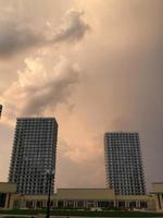 two tall residential apartment buildings, poles in the city center. houses of a new format, white, without a balcony with a glass terrace. against the background of the sunset, peach sky photo