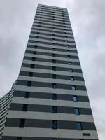 tall residential building in the form of a column of blue and white color in the city center. there are many small rectangular windows on the house. house on the background of the cloudy sky photo