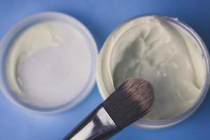 A beauty box with a wooden brush made from natural hard lint for a tone and a round jar of cream, a make-up base with a second skin effect on a blue background. Flat lay. Top view photo
