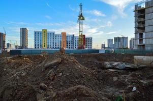 construcción de un nuevo barrio. una gran grúa está cavando un foso de arena para la futura fundación. en el contexto de un edificio de varios pisos brillante, colorido y multicolor. foto