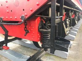 Large iron wheels of a red and black train standing on rails and suspension elements with springs of an old industrial steam locomotive photo