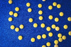 Small yellow orange beautiful medical pharmaceptic round pills, vitamins, drugs, antibiotics on a blue background, texture. Concept medicine, health care. Flat lay, top view photo