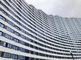 an unusual panoramic image of a house of different heights. residential apartment building in the form of a wave of blue and white. small windows, street lamps. against the background of  cloudy sky photo