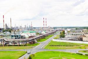 Industrial landscape. Panoramic view of the technological pipes. Plant settings. From the chemical red-white pipes smoke is coming. Production buildings. Against background of sky and bright grass photo