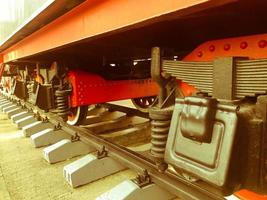 grandes ruedas de hierro de un tren rojo y negro parado sobre rieles y elementos de suspensión con resortes de una vieja locomotora de vapor industrial foto