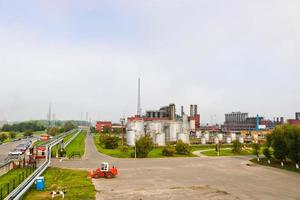 paisaje industrial con plantas químicas, tuberías y columnas. abajo hay un tractor naranja. sale humo del reactor. vista panorámica de la producción de reparación. tuberías de proceso foto