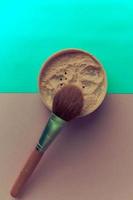 Beauty box, crumbly matte mineral powder with a special brown beautiful wooden brush from natural nap for makeup on a warm green and brown background. Flat lay. Top view photo