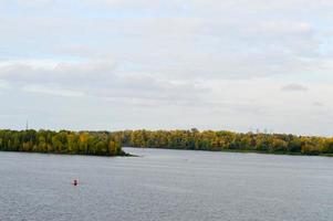 A lonely red buoy floats against the background of trees on the shore. Landscape. photo