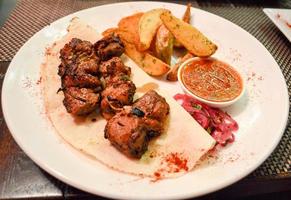 brochetas de ternera con patatas en un plato blanco foto