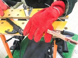 A welder man in red work gloves is working and holding an electron and clamps for welding at the table photo