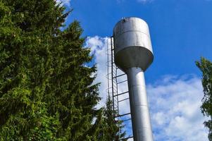 gran torre de agua industrial de acero inoxidable brillante para suministrar agua de gran capacidad, barril contra el cielo azul y los árboles