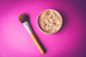 Beauty box, crumbly matte mineral powder with a special brown beautiful wooden brush from natural nap for makeup on a warm pink purple background. Flat lay. Top view photo