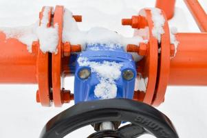 Industrial shut-off regulating protective pipe fittings. Black valve for opening, closing on an iron orange metal pipe with flanges, studs, nuts against the background of white snow in winter photo