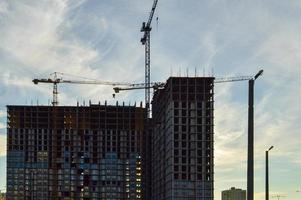 a concrete multi-storey building is being built in the city center. the builders have inserted many windows, the house stands next to lampposts and a construction crane. construction of a new area photo