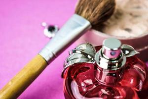 Beauty box, crumbly matte mineral powder with a special natural brown wooden brush from natural nap for make-up, pink perfume and shiny silver earrings on a pink purple background photo