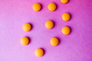 Small yellow orange beautiful medical pharmaceptic round pills, vitamins, drugs, antibiotics on a pink purple background, texture. Concept medicine, health care. Flat lay, top view photo