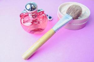 Beauty box, crumbly matte mineral powder with a special natural brown wooden brush from natural nap for make-up, pink perfume and shiny silver earrings on a pink purple background. Flat lay. Top view photo