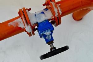 Industrial shut-off regulating protective pipe fittings. Black valve for opening, closing on an iron orange metal pipe with flanges, studs, nuts against the background of white snow in winter photo