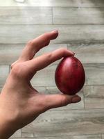 Easter egg of burgundy shiny color, with glitter in female hands with pink manicure. paint the shell with onion peel. Easter basket for a gift to a rabbit. chicken egg in color on a wood background photo