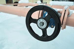 Industrial shut-off regulating protective pipe fittings. Black valve for opening, closing on an iron orange metal pipe with flanges, studs, nuts against the background of white snow in winter photo