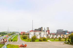 paisaje industrial con plantas químicas, tuberías y columnas. abajo hay un tractor naranja. sale humo del reactor. vista panorámica de la producción de reparación. tuberías de proceso foto