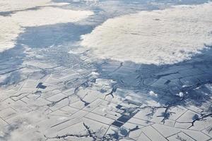 Aerial cloudscape view over clouds top to snow covered rivers, roads, cities and fields, winter air photo