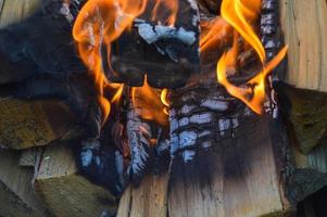 tablones de madera quemados calientes carbonizados de troncos de madera en un fuego con lenguas de fuego y humo. textura, fondo foto