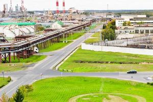 Industrial landscape. Panoramic view of the technological pipes. Plant settings. From the chemical red-white pipes smoke is coming. Production buildings. Against background of sky and bright grass photo