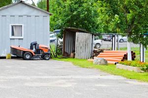 A large professional agricultural lawn mower, a lawn mowing tractor with grass, stands near the tool shed photo