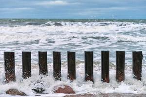 altos rompeolas de madera en olas de mar espumoso y cielo nublado foto