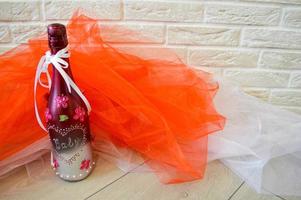 A homemade bottle of champagne decorated with a heart pattern, baby lettering and flowers on a background of red and white fabric and a brick wall. photo