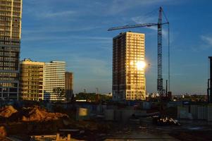 construction of new high houses. a glare of the sun is visible in the window. cranes stacking blocks to build a new floor.  building materials under the film. skyscrapers in the city center photo