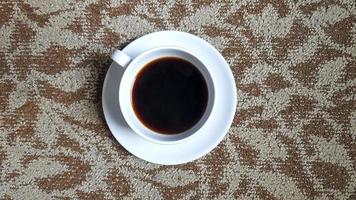 vista superior de una taza blanca de café negro sobre alfombra marrón o fondo de alfombra con espacio para copiar. endecha plana de bebida caliente sobre papel tapiz de suelo de algodón.