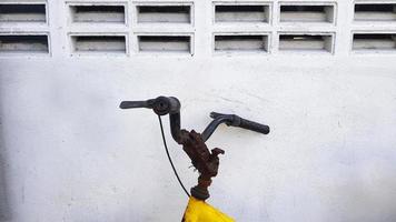 Close up rusty bicycle handlebar lean and isolated on white concrete wall with copy space. Old object and Transportation. Yellow Stainless steel handle of bike. photo