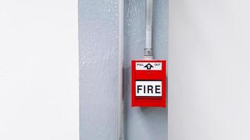 Red fire alarm button for pull out in emergency case happen in stalled on gray or grey steel pole with white wall background and copy space. Warning equipment or tool.