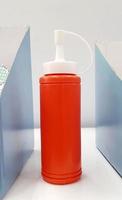 Orange ketchup or tomato sauce on white shelf for sale. Plastic container and new bottle object. photo