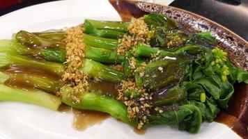 Hong Kong kale with oyster sauce and dried garlic topping on white dish or plate at Chinese restaurant. Delicious Asian food. photo