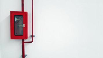 caja roja de acero inoxidable que contiene el abridor de válvulas de agua para la lucha contra incendios con tubería de agua o tubería en la pared blanca con espacio de copia a la derecha. caja de seguridad y equipo de protección en caso de emergencia c foto