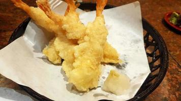 Close up Tempura with Garlic smoothie on white oil paper on black basket at Japanese restaurant. Deep fried shrimp or prawn in Japan style. Asian food and snack before eat main meal. photo
