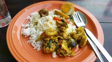 Thai food with spicy chicken yellow curry, brinjal and stewed Egg on white rice with fork and spoon on orange dish or plate at local street food. Breakfast or Lunch for people in Thailand eat. photo