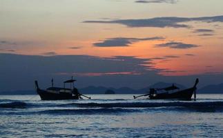 dos siluetas de bote de cola larga en el mar y olas con cielo naranja y fondo de nubes en krabi, tailandia. paisaje del océano al atardecer. foto