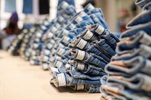 Denim jeans stack on wood table in clothing store, shopping photo