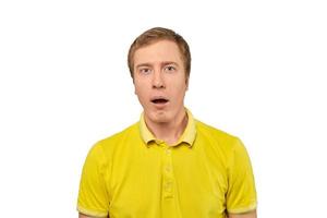 Puzzled young man with funny face and open mouth in yellow Polo T-shirt, white isolated background photo