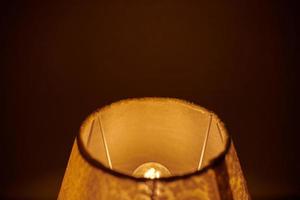 Incandescent lamp in round lampshade glowing in dark. photo