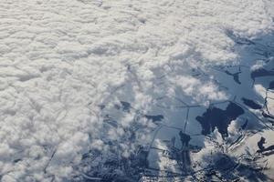 Aerial view over clouds top to snow covered rivers, fields and roads, winter fresh frosty air photo