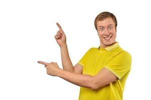 Surprised guy with funny face in yellow Polo T-shirt pointing finger to left, white background photo