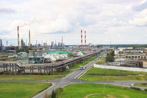 Industrial landscape. Panoramic view of the technological pipes. Plant settings. From the chemical red-white pipes smoke is coming. Production buildings. Against background of sky and bright grass photo